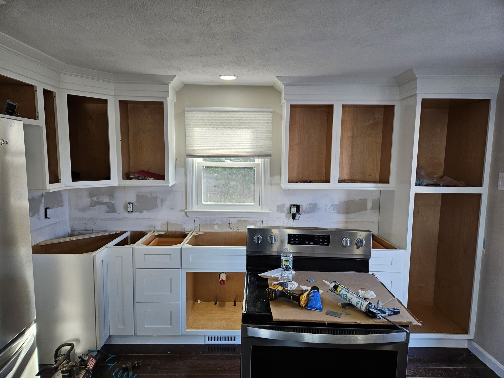Partially renovated kitchen with white cabinets, wood paneling, stove, sink, and tools on the counter