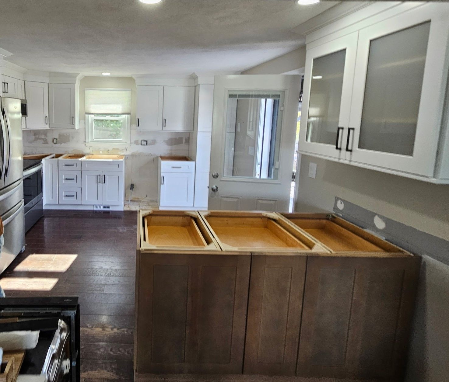 Bright white kitchen with dark wood floors, gray cabinets, and a large island under renovation.