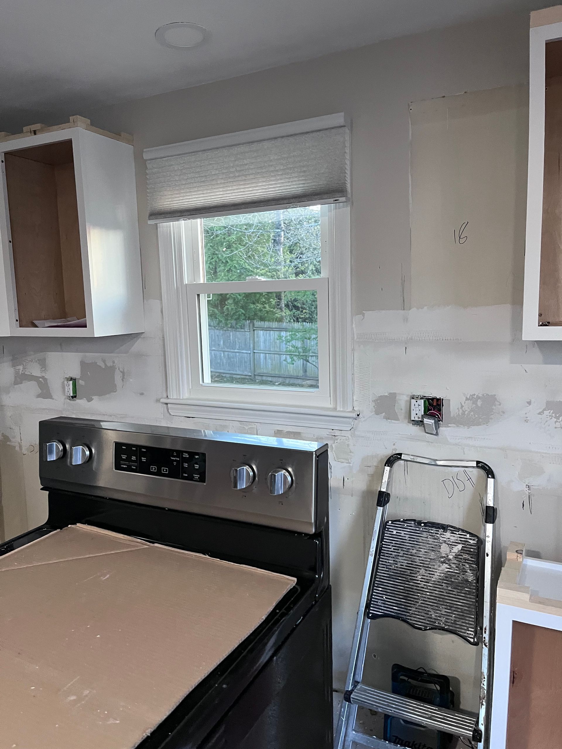 Kitchen with white cabinets, window, and a black stove covered with cardboard during renovation