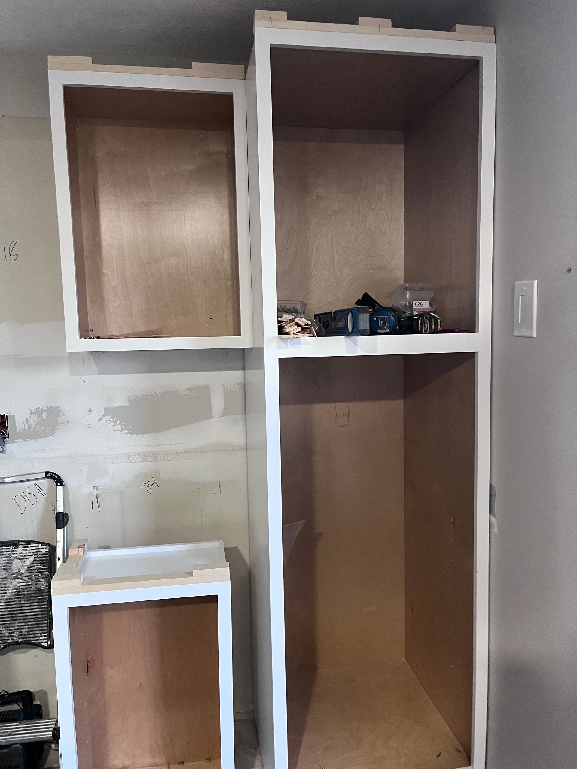 Unfinished built-in wall shelves and cubbies, white trim with brown interiors, in a room under renovation