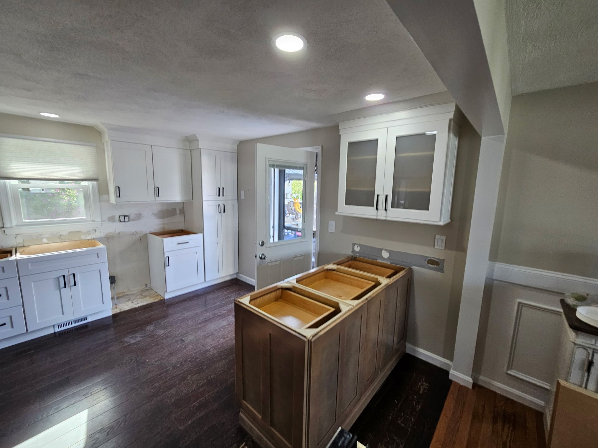 Bright kitchen with white cabinets, dark wood floor, and a central island under recessed lights