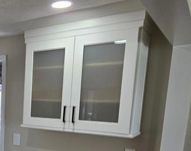White kitchen wall cabinet with frosted glass doors and black handles above a countertop