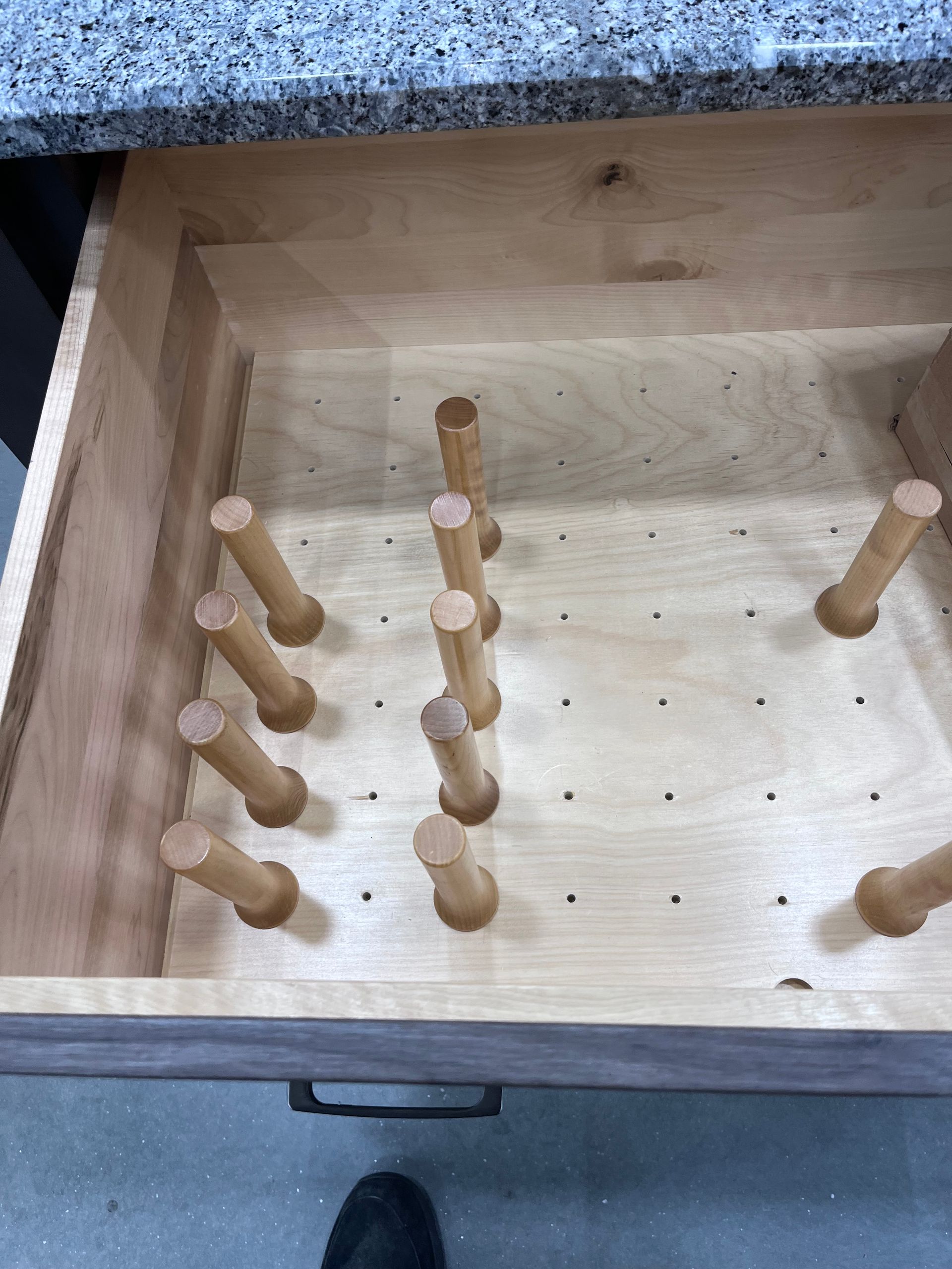 Wooden peg game board with several light wood pegs arranged in rows inside a square tray.