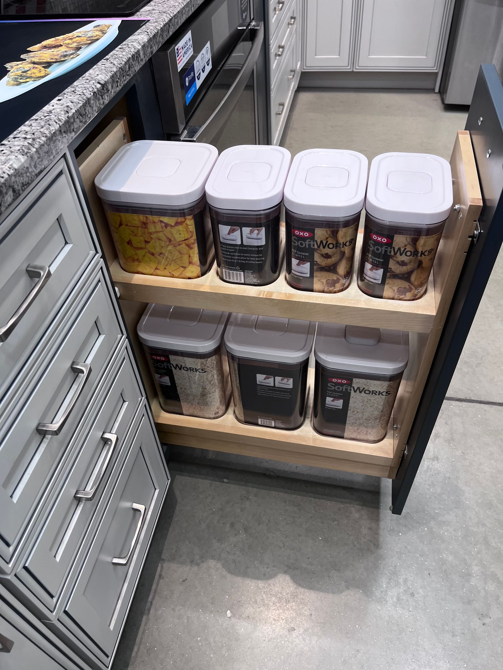 Pull-out pantry drawer with labeled plastic food containers in a kitchen.