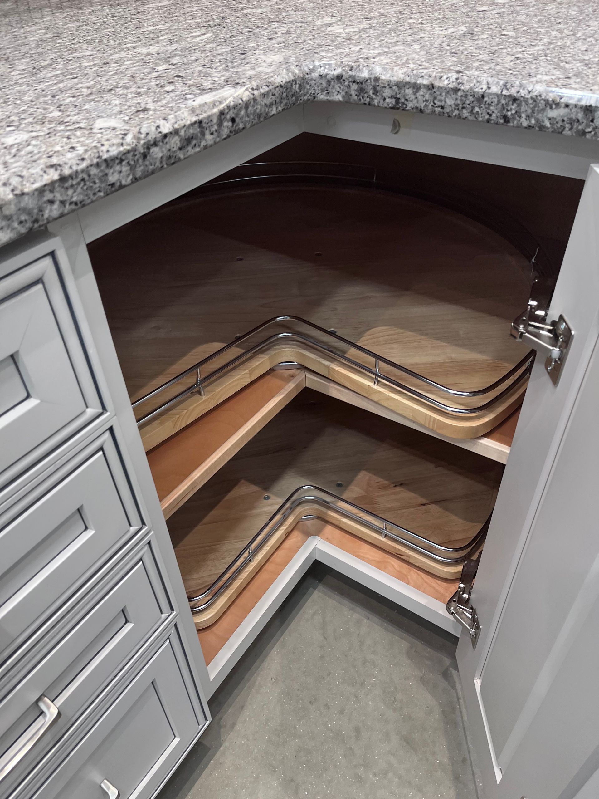 Open corner cabinet with pull-out shelves in a kitchen, showing wood shelving and gray doors.