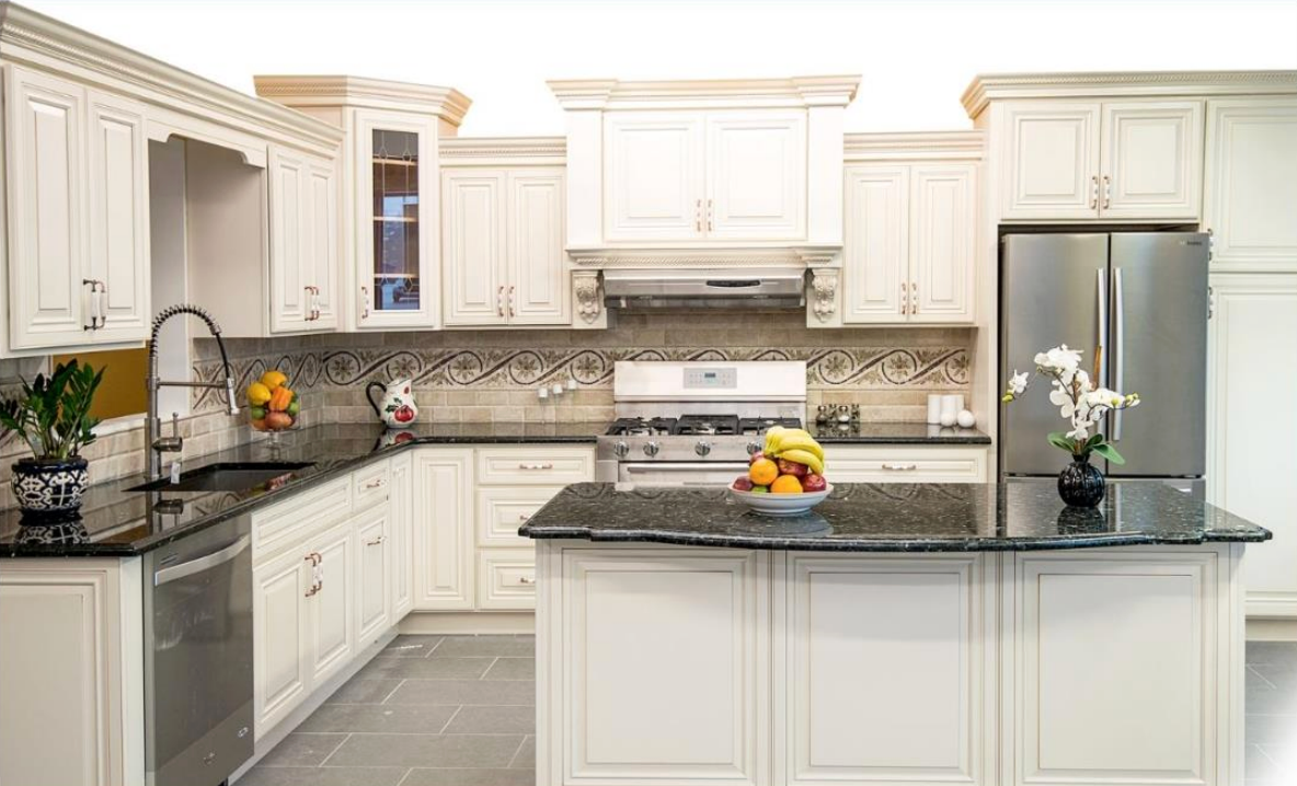 Bright white kitchen with dark granite counters, island, stainless steel appliances, and fruit centerpiece