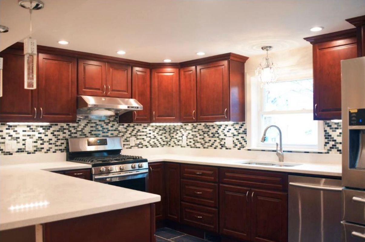Modern kitchen with dark wood cabinets, white countertops, stainless stove, and mosaic tile backsplash.