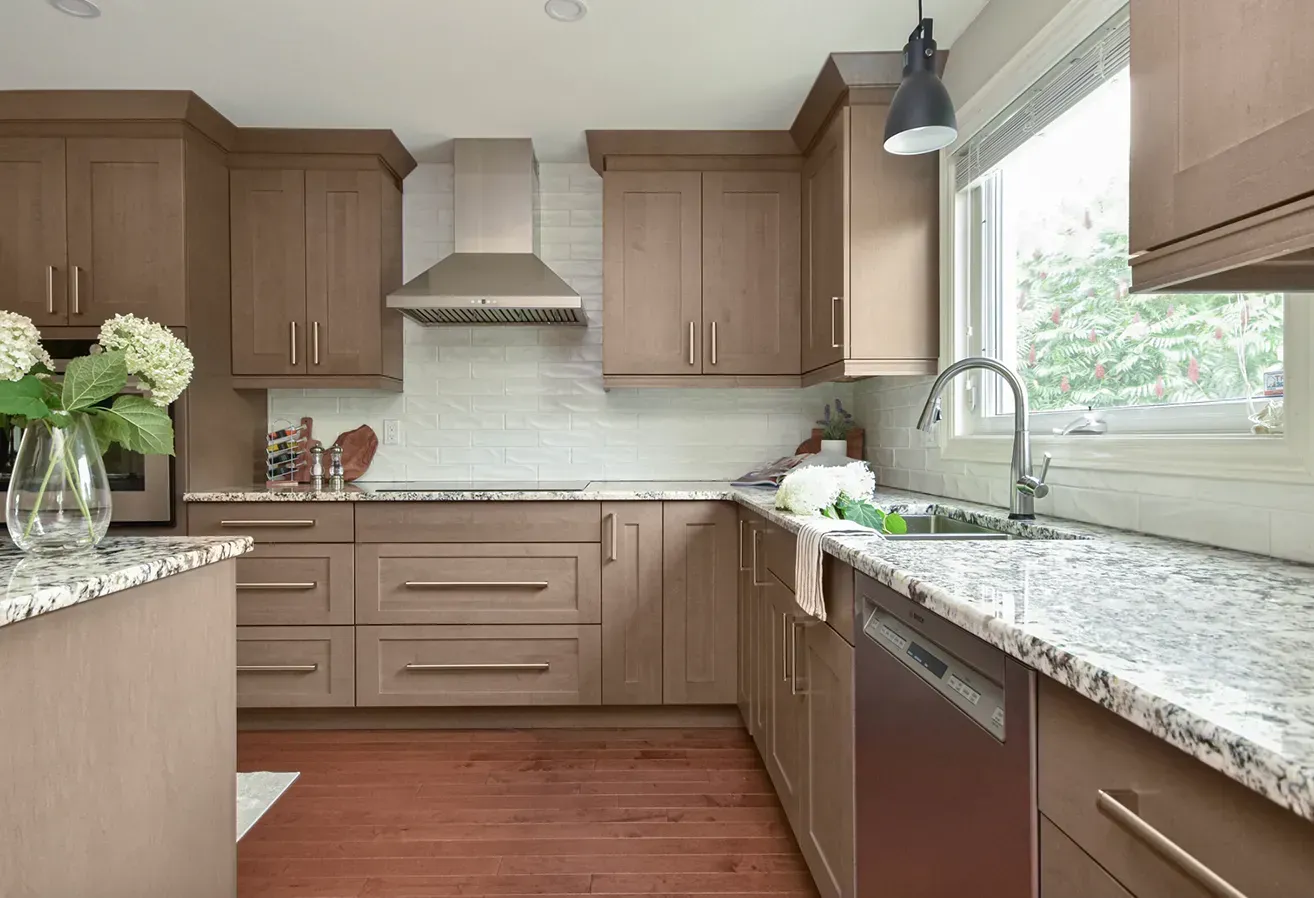 Modern kitchen with brown cabinets, granite countertops, stainless range hood, and a window over the sink.