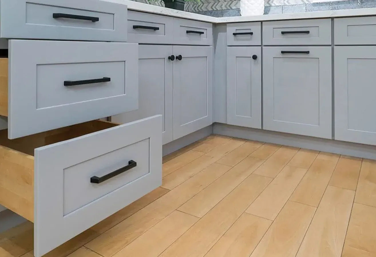 Open kitchen cabinet drawers with gray fronts and black pulls on a light wood floor