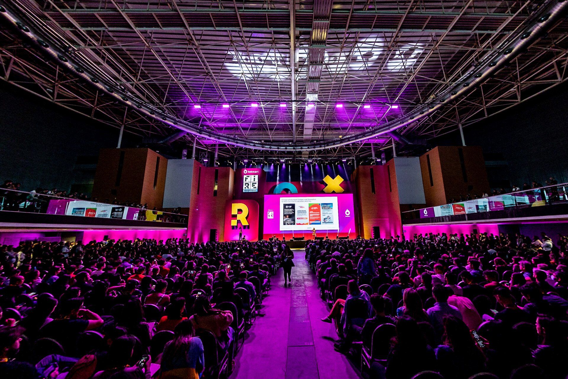 A large crowd of people are sitting in front of a stage with purple lights.