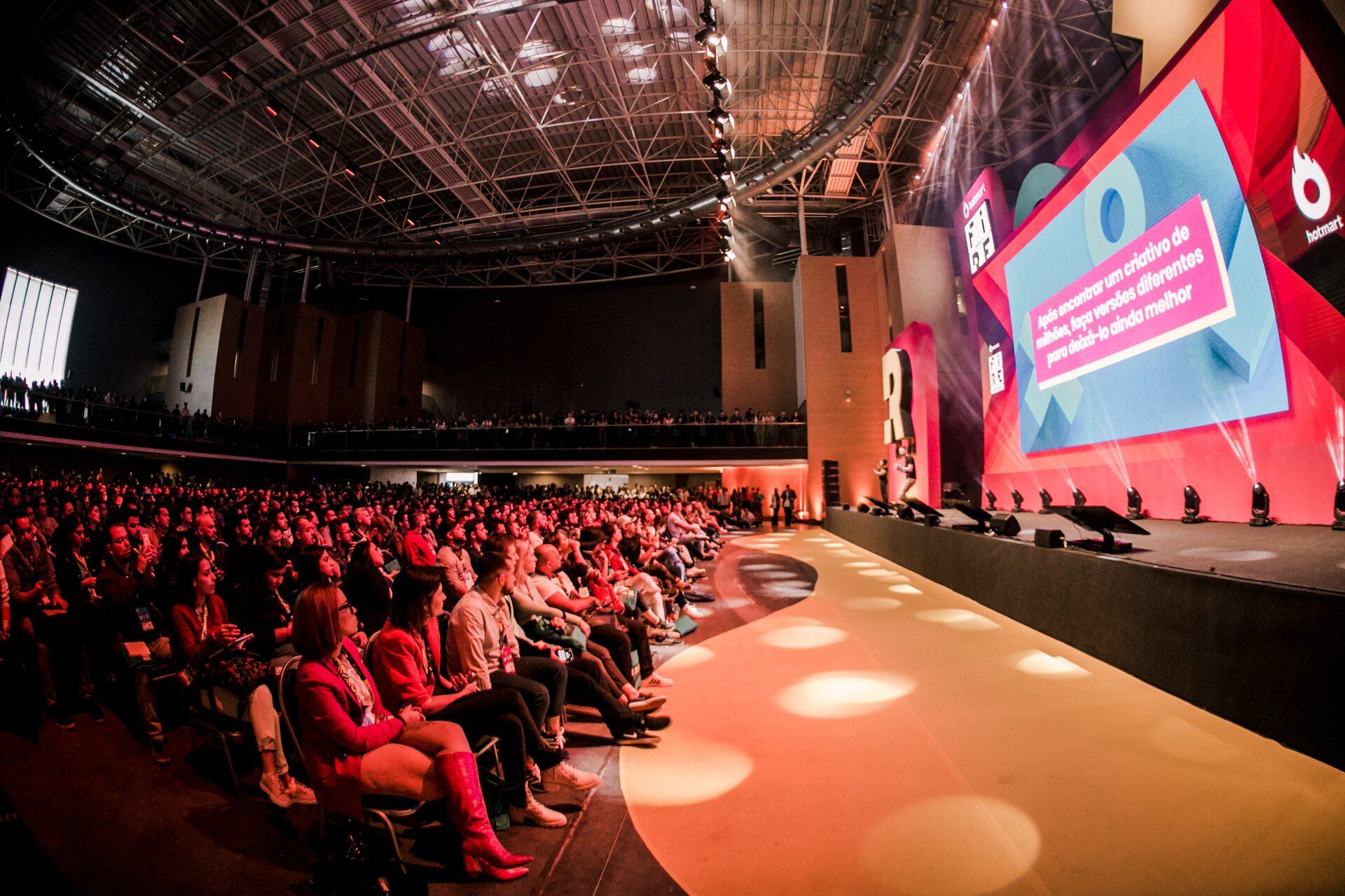 A large crowd of people are sitting in a large auditorium watching a presentation.