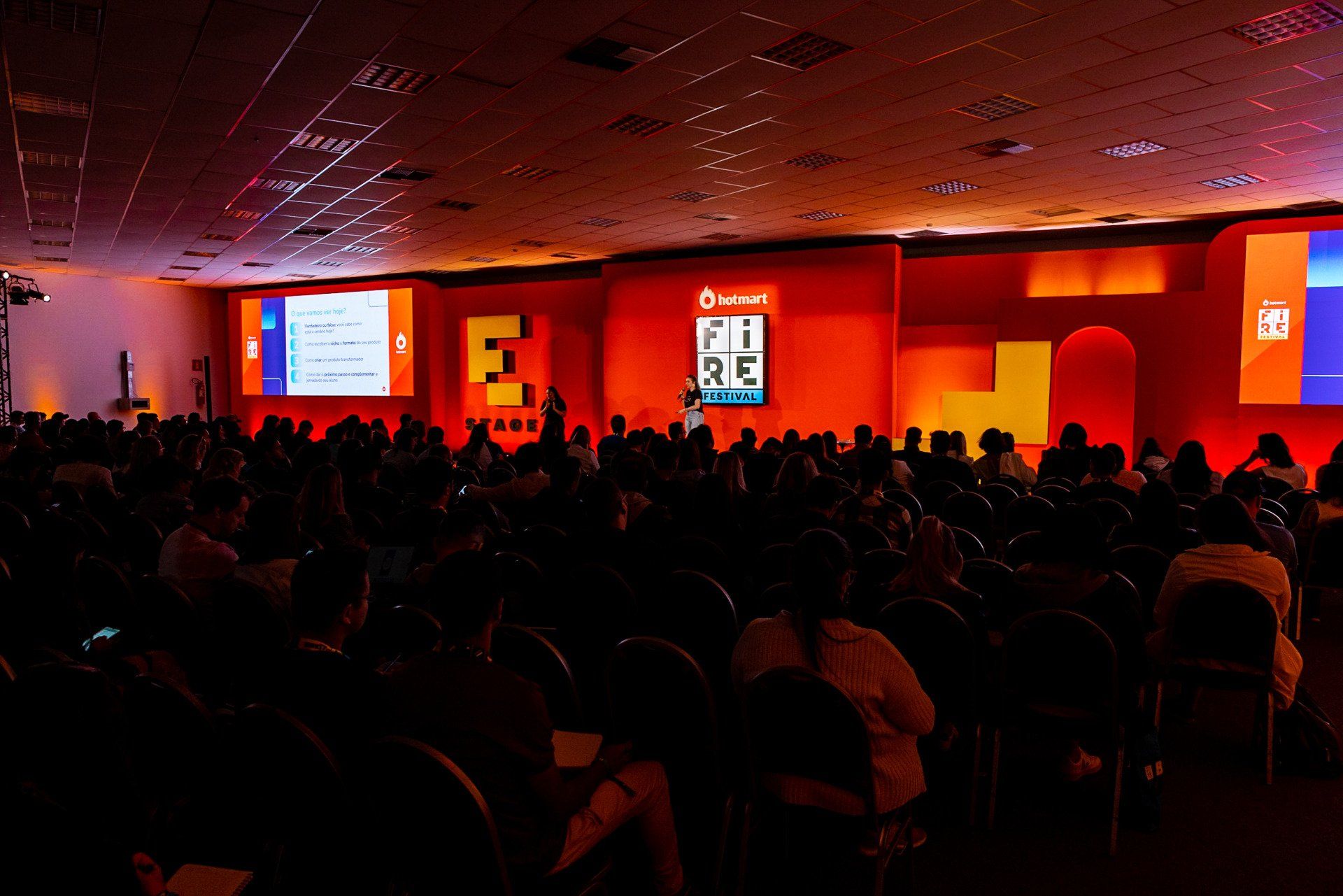 A large group of people are sitting in a dark auditorium watching a presentation.