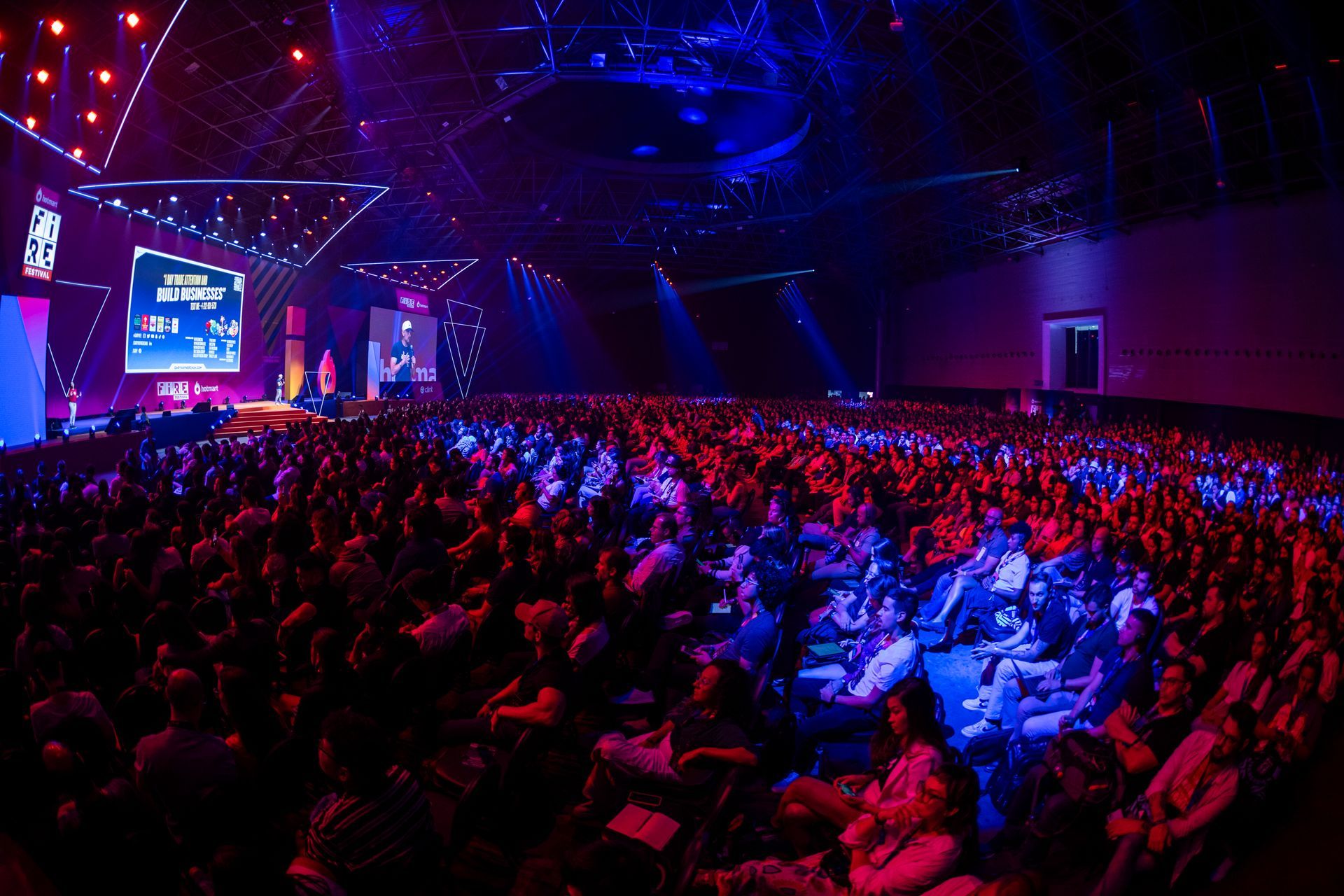 A large crowd of people are sitting in a large auditorium watching a presentation.