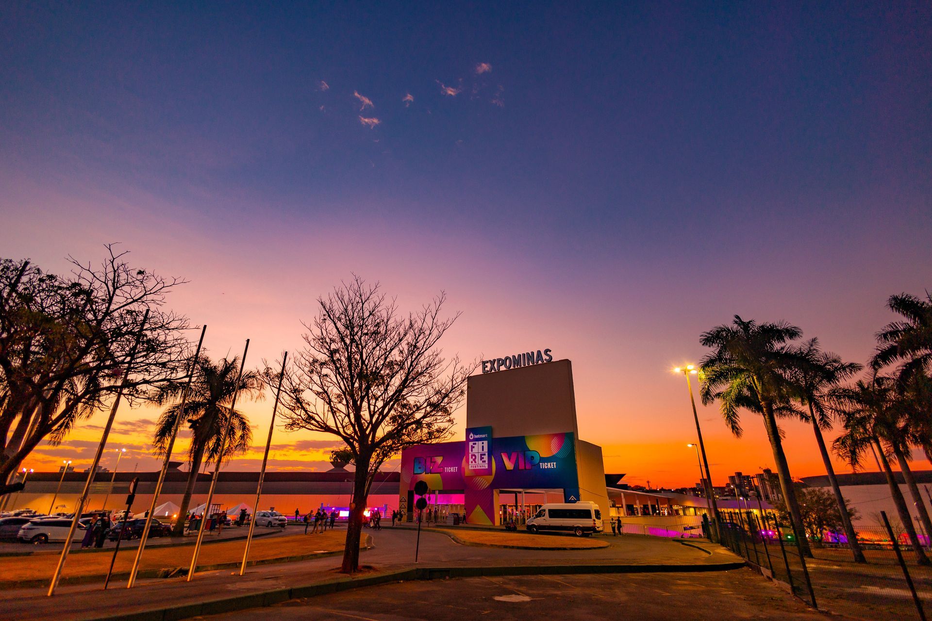 A sunset over a parking lot with palm trees and a building in the background.