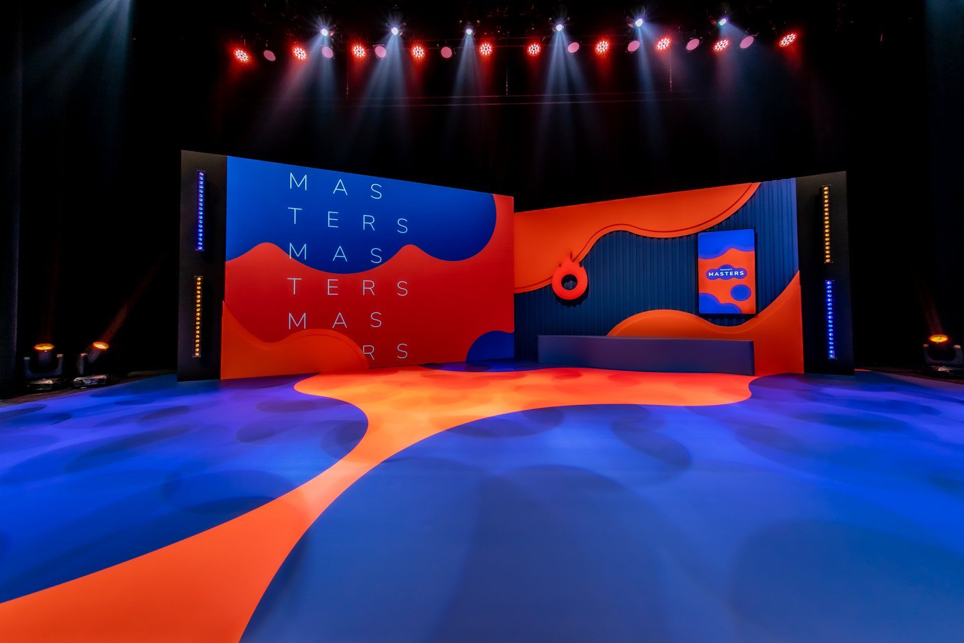 Un escenario con una alfombra azul y naranja y una gran pantalla detrás.