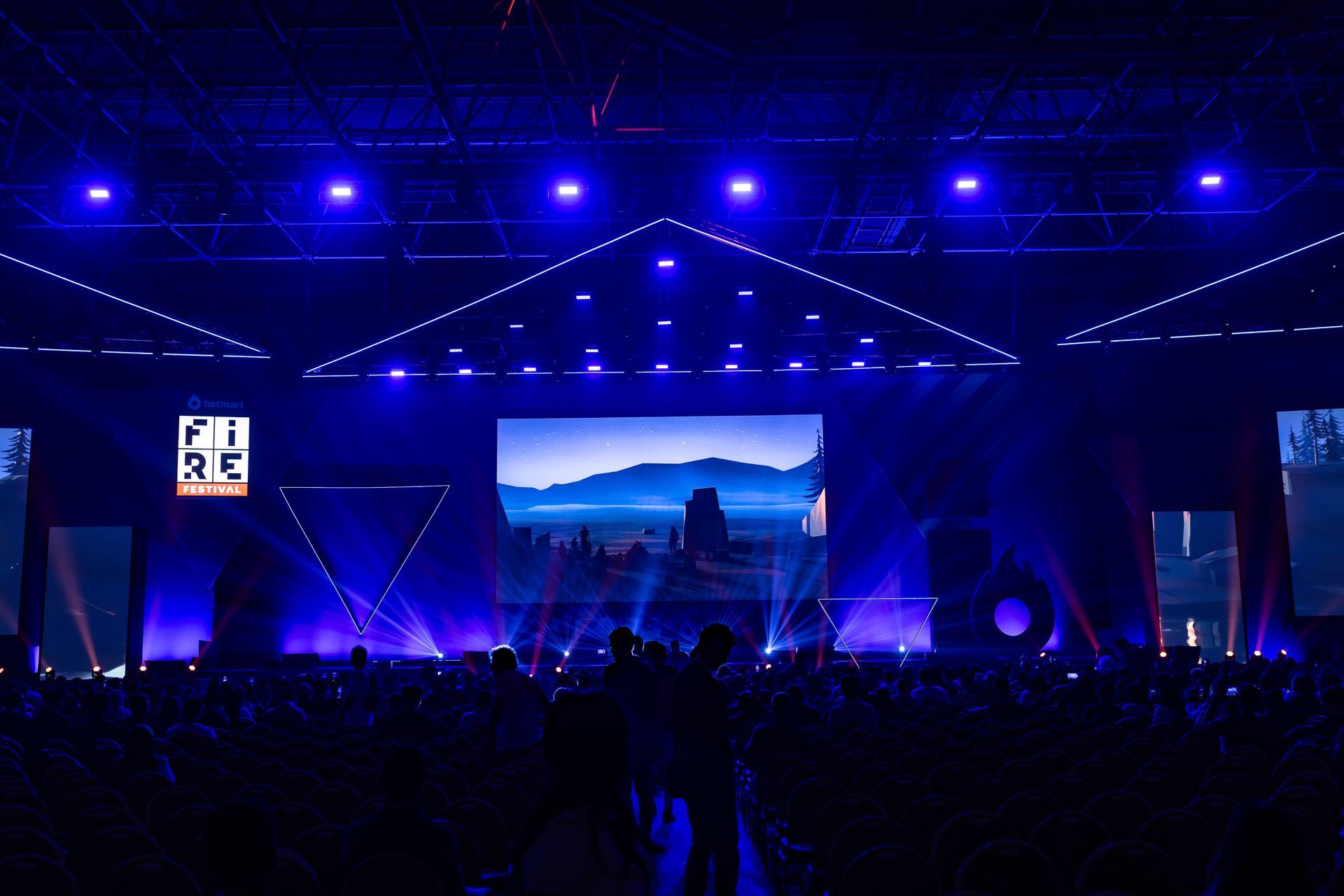 A crowd of people are gathered in front of a stage with a large screen that says re