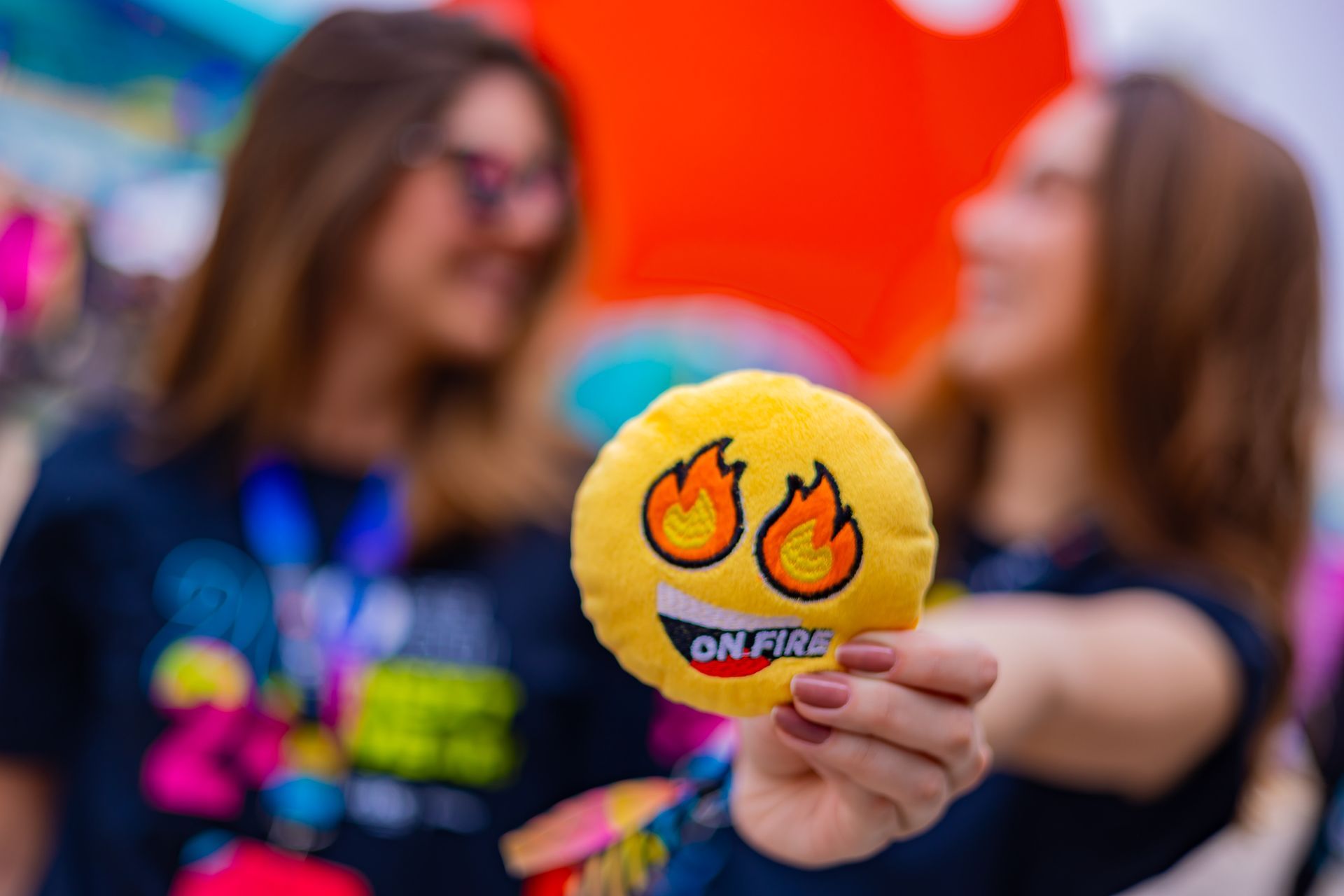 A woman is holding a stuffed smiley face with flames on it.