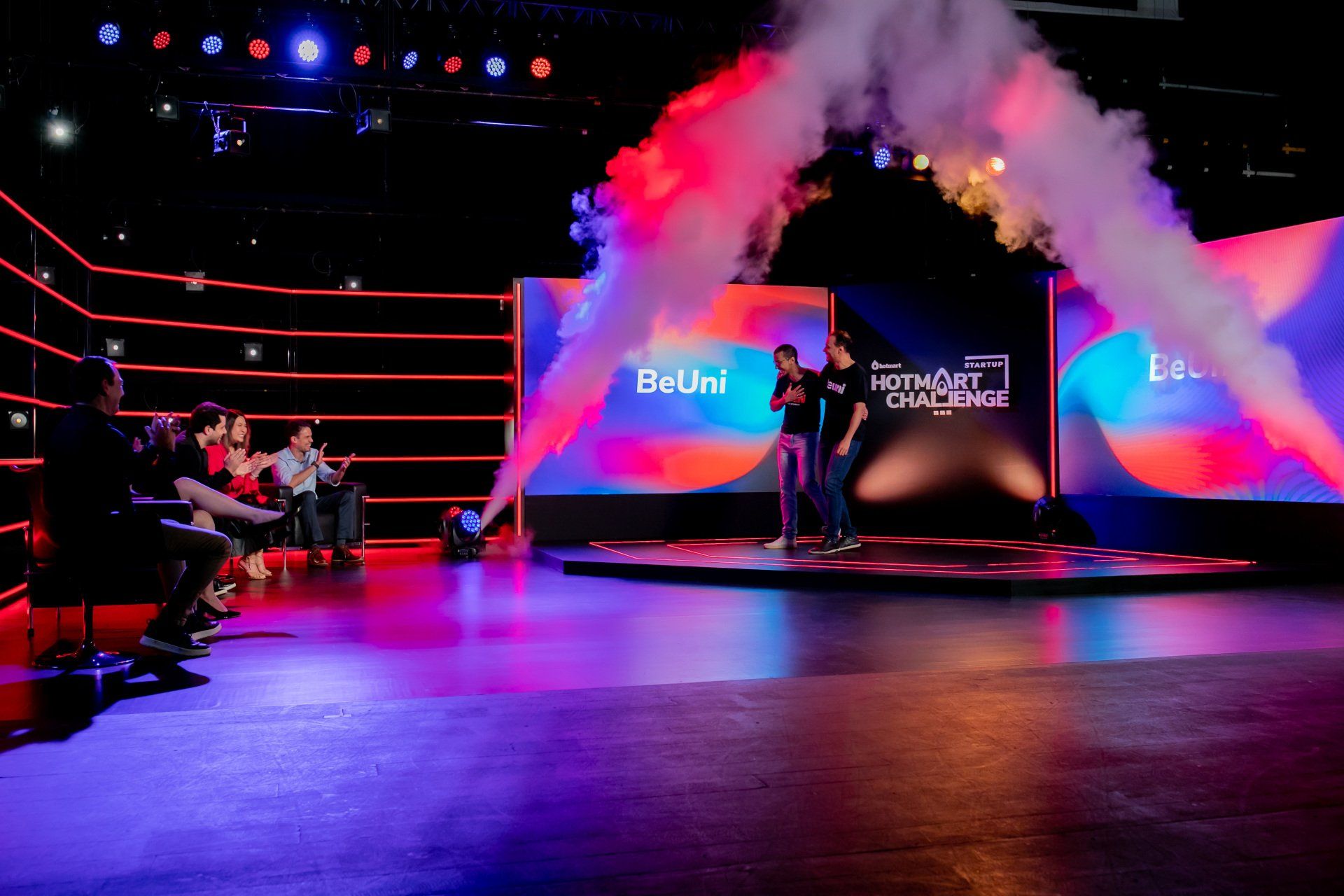 Um grupo de pessoas está sentado em frente a um palco com fumaça saindo dele.