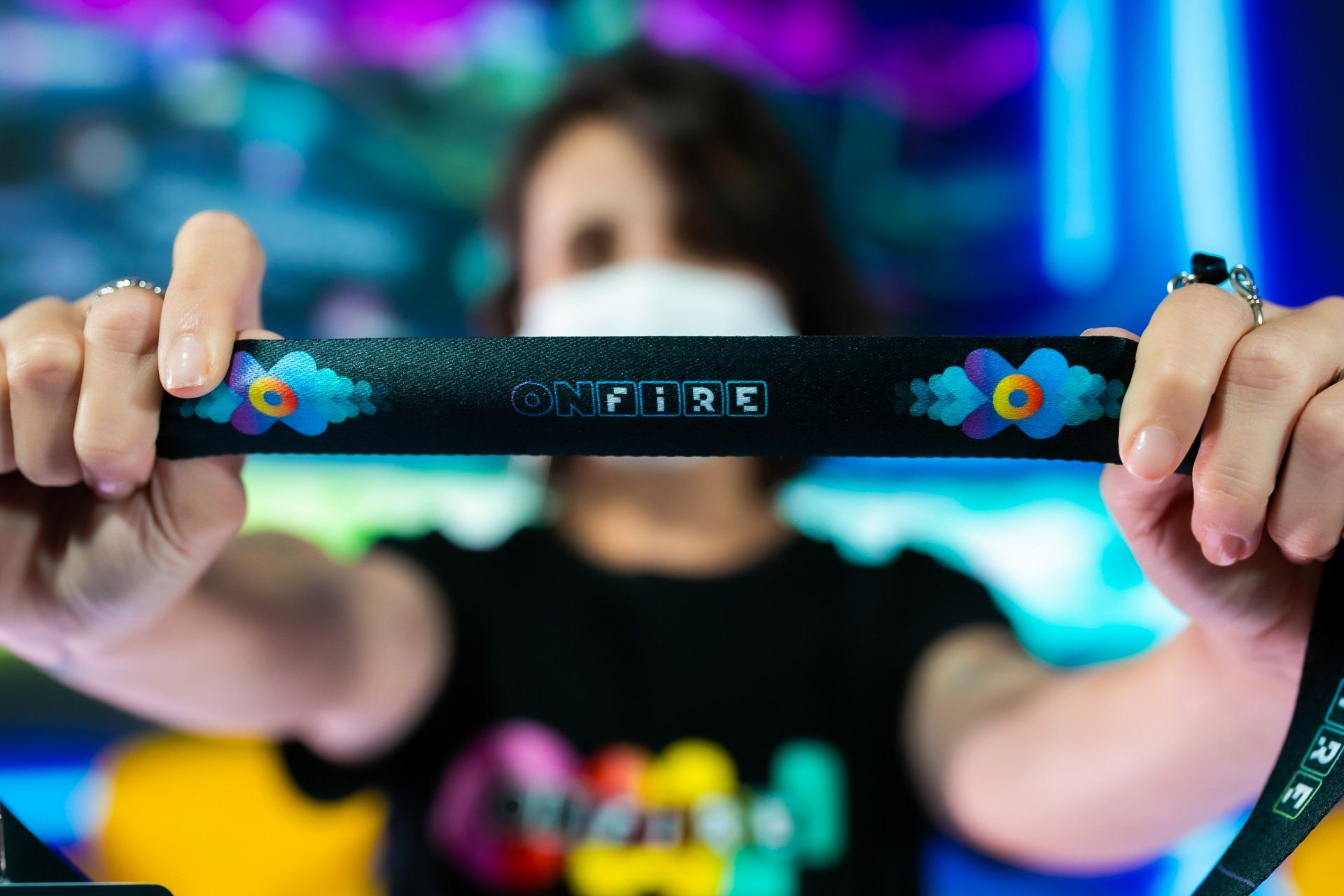 A woman wearing a mask is holding a lanyard with the word spitfire on it.