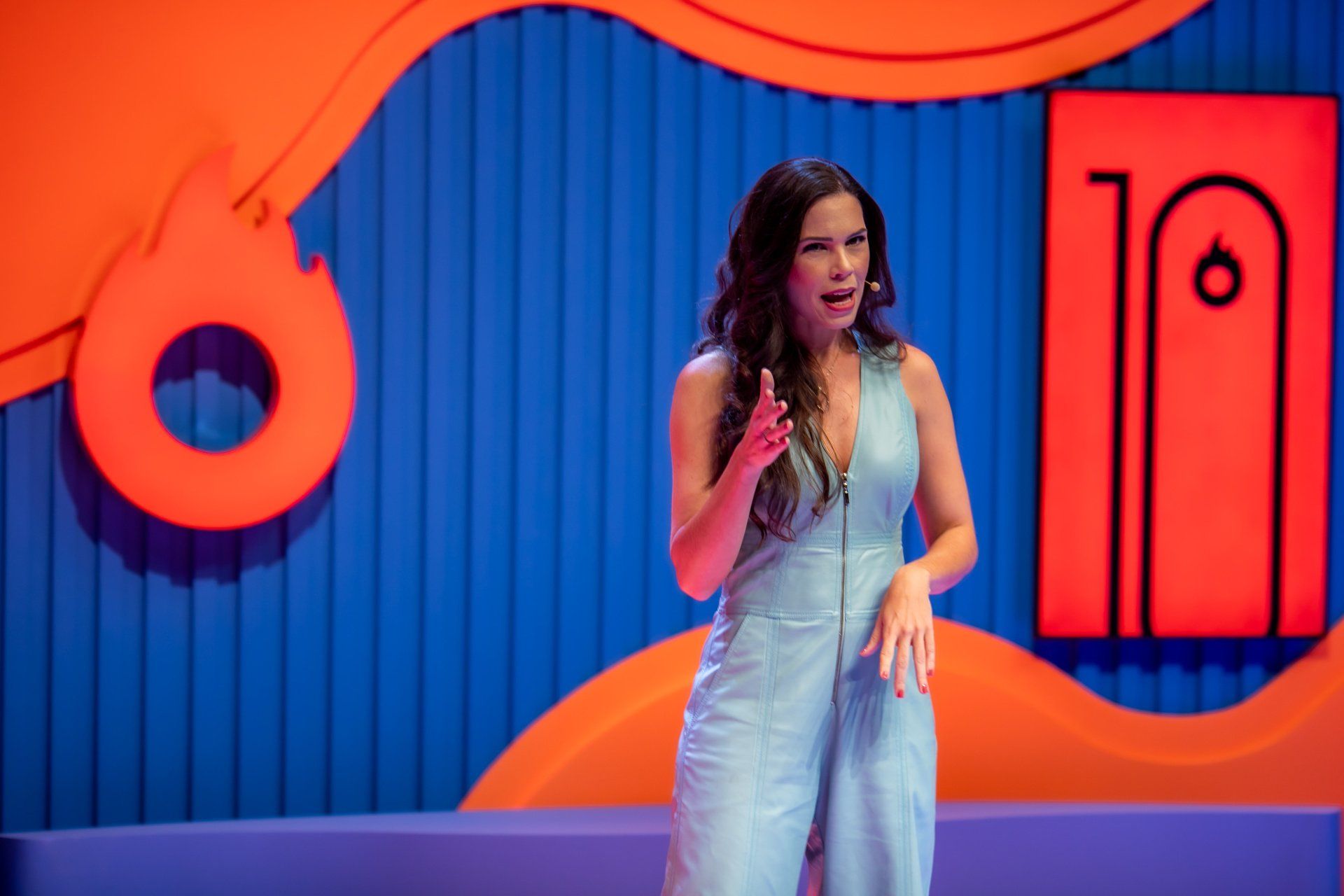A woman in a blue jumpsuit is standing in front of a microphone on a stage.