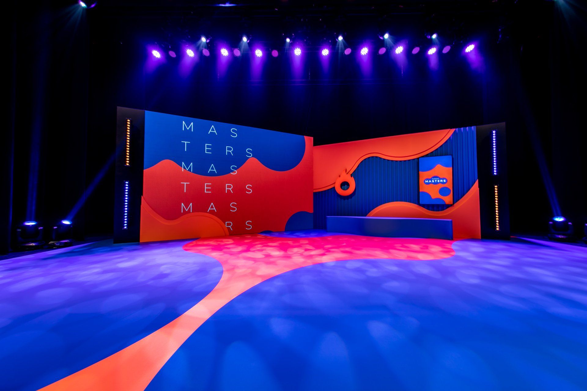A stage with a blue and orange carpet and a large screen.