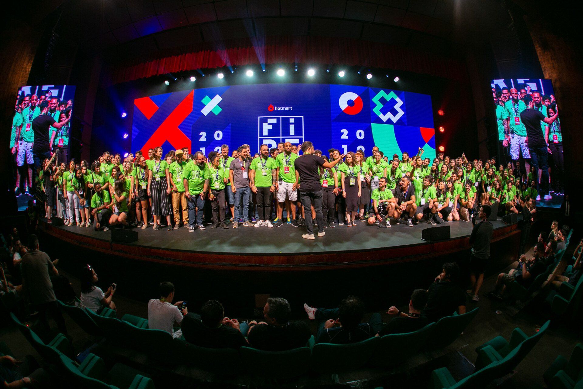 A large group of people are standing on a stage in front of a large screen.