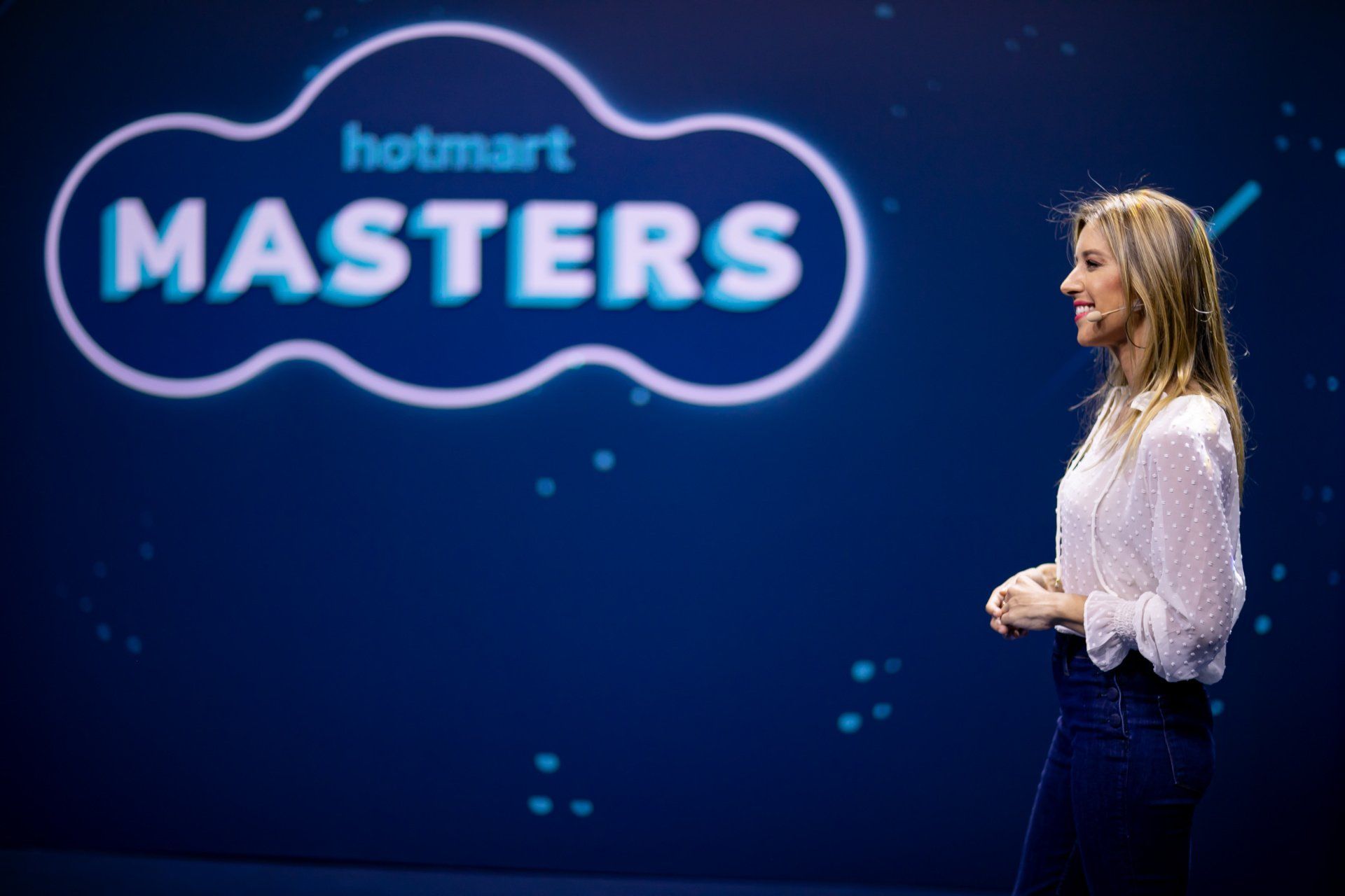 A woman is standing in front of a sign that says hotmart masters.
