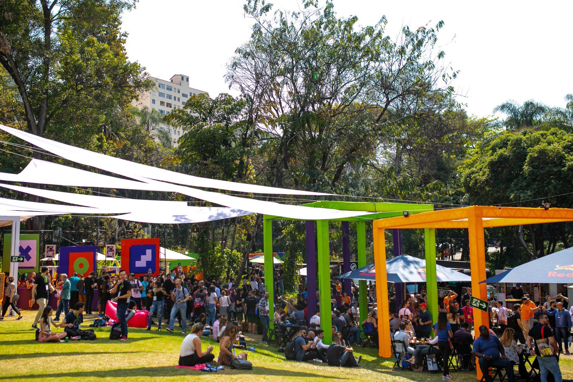 A large group of people are sitting under umbrellas in a park.