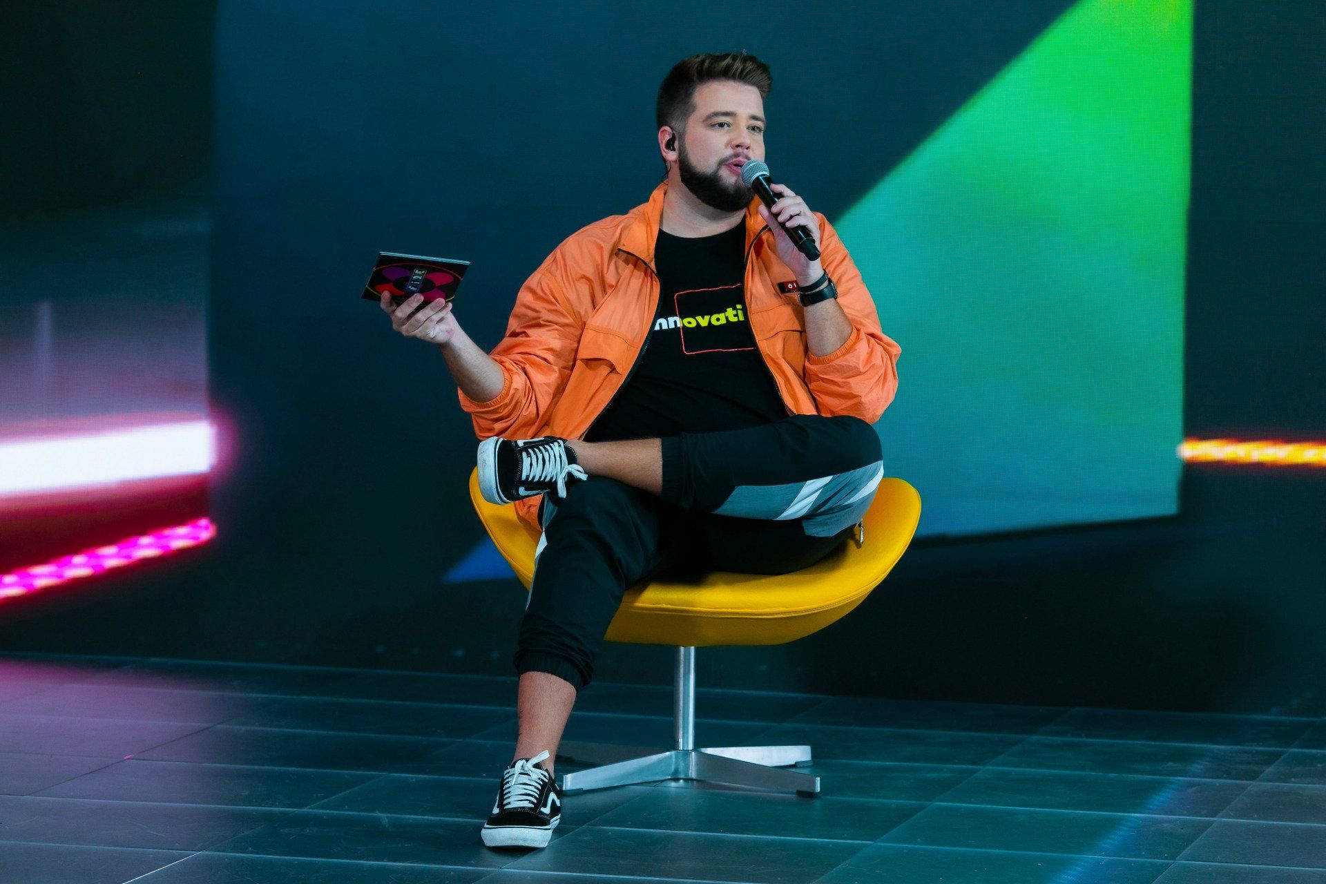 A man is sitting in a yellow chair holding a microphone.