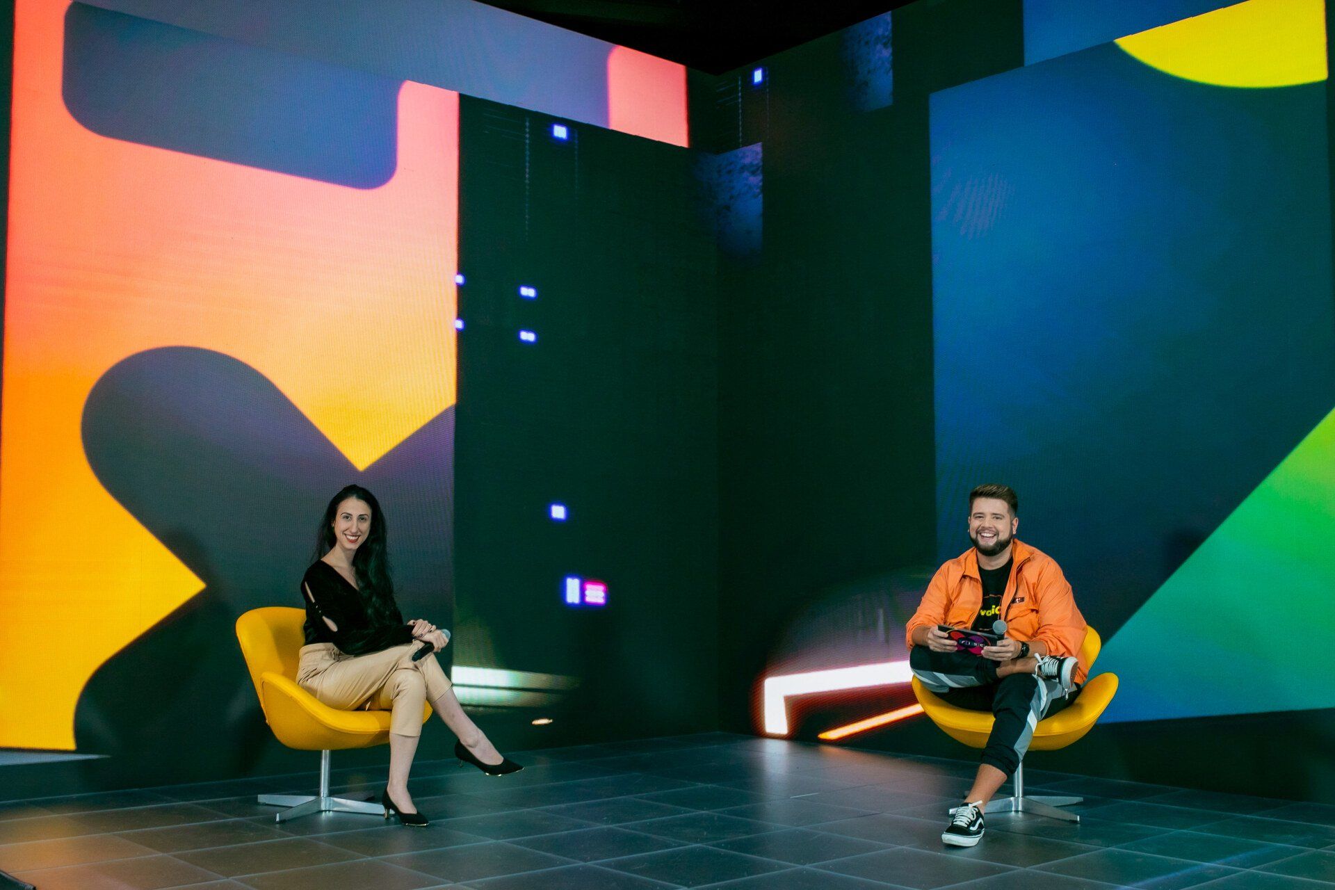 A man and a woman are sitting in chairs in front of a large screen.