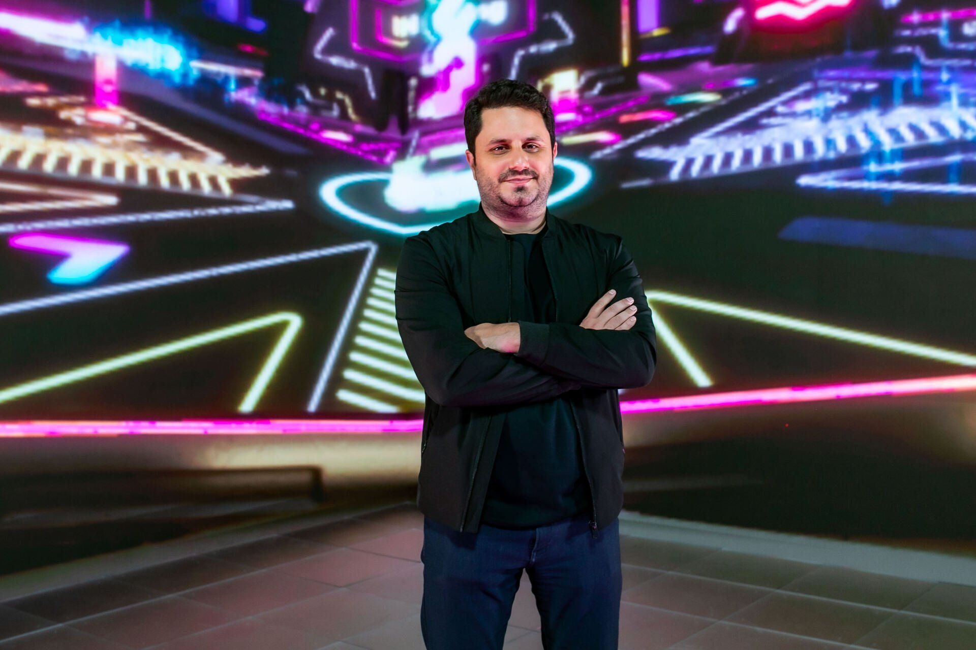 A man is standing in front of a large screen with his arms crossed.