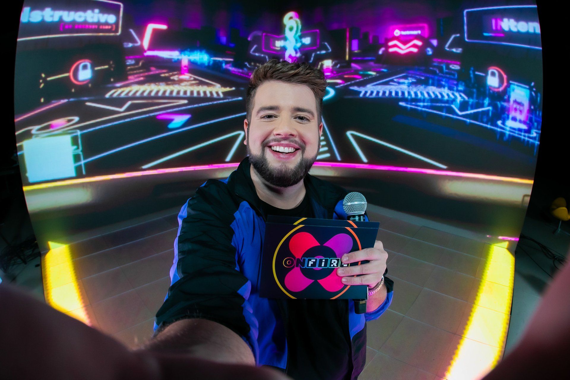 A man is taking a selfie in front of a screen while holding a microphone.