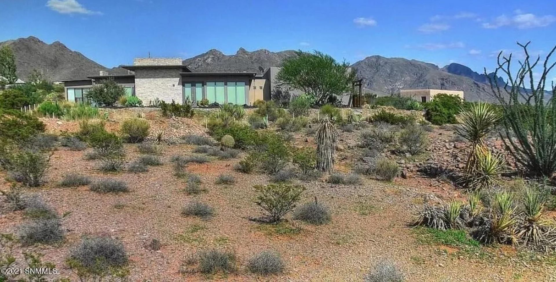 A house in the middle of a desert with mountains in the background.