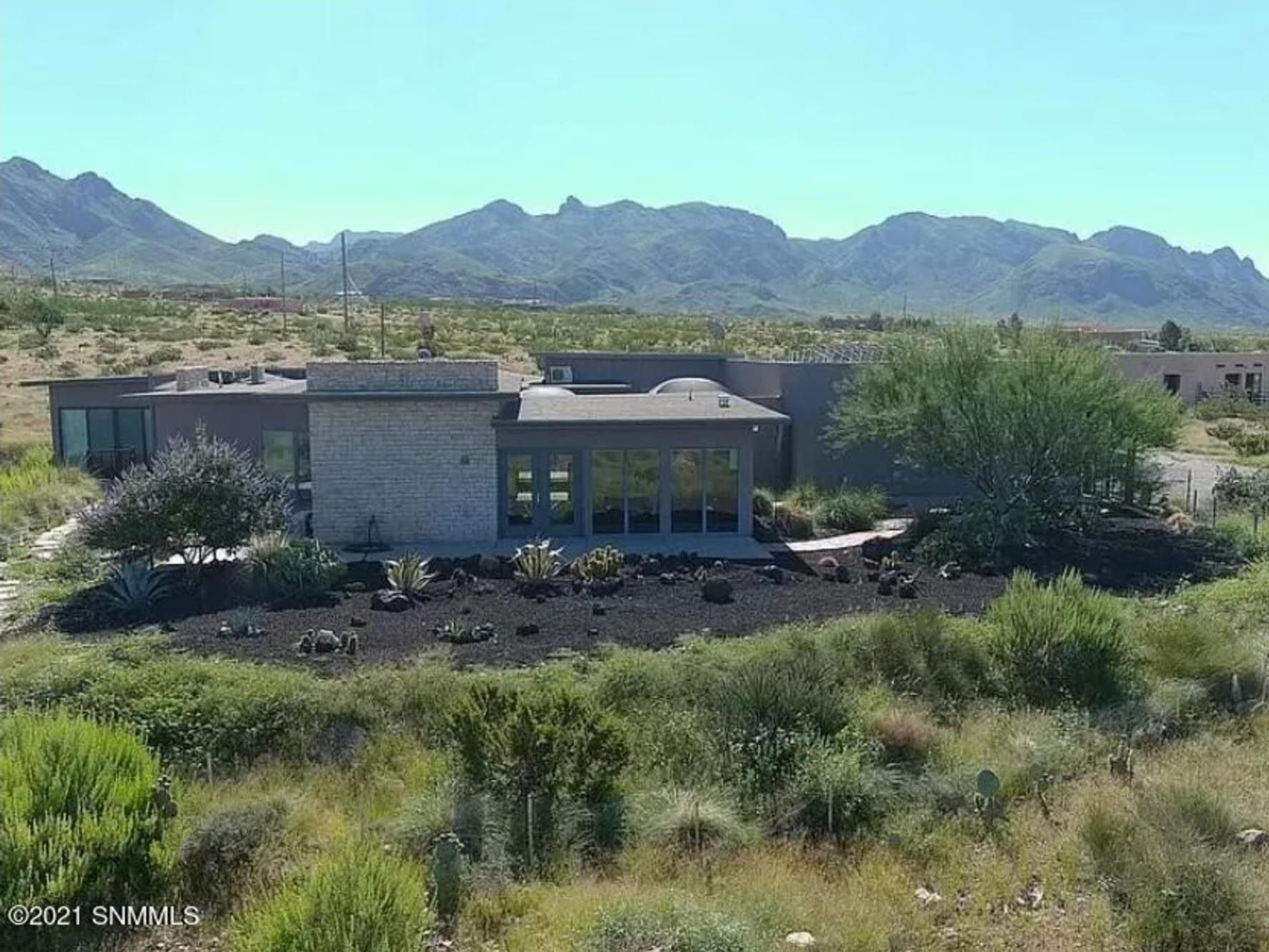 An aerial view of a house in the desert with mountains in the background.