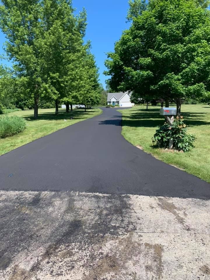 A driveway leading to a house surrounded by trees and grass.