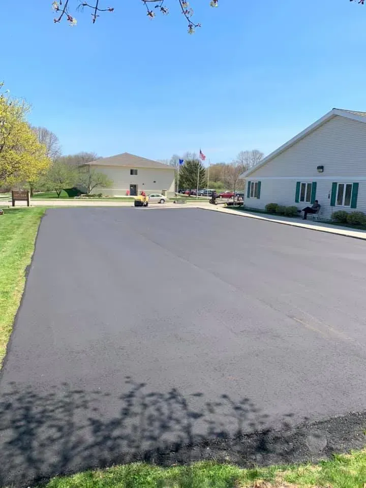 A large asphalt driveway is being paved in front of a building.