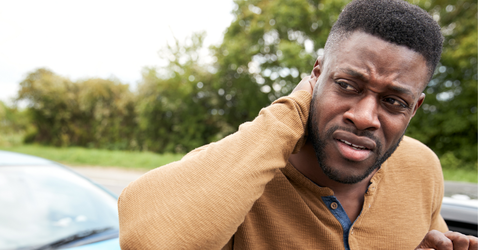A man is holding his neck in pain in front of a car.