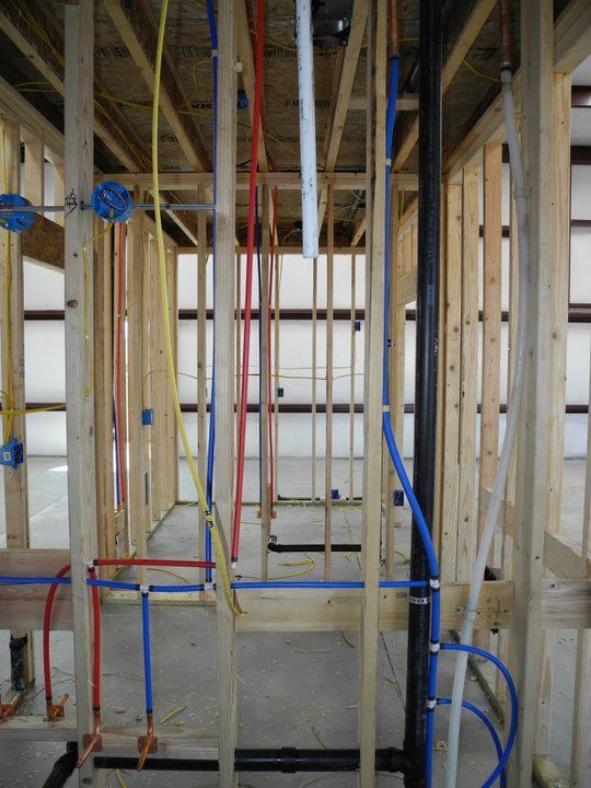 Wooden frame of a building with visible red, blue, yellow, and black pipes for plumbing and electrical wiring.