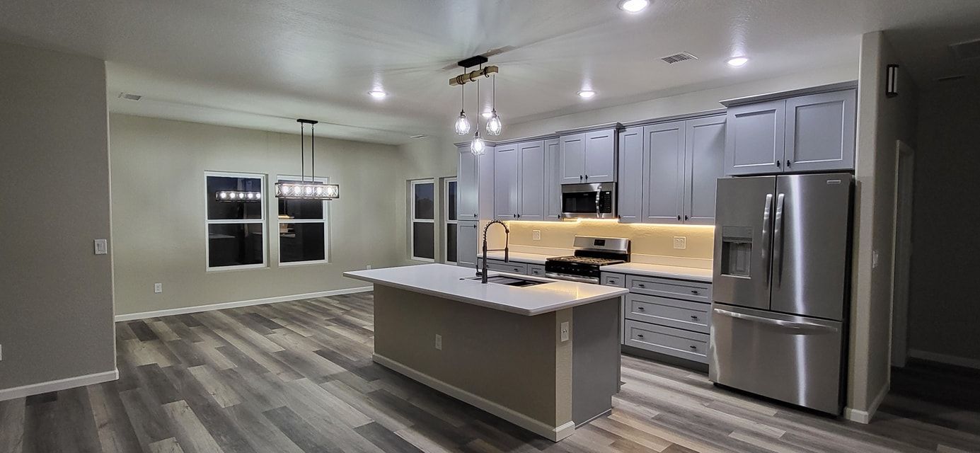 Kitchen with gray cabinets, island, stainless steel refrigerator, and wood-look flooring.