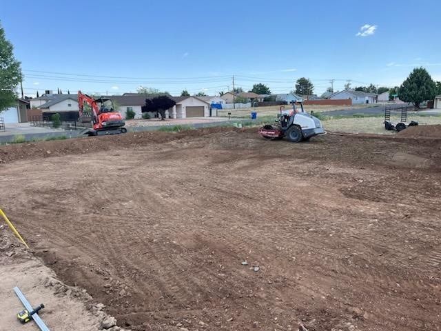 Construction site with excavator and roller compacting soil under a blue sky.