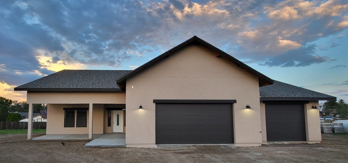 A light beige house with a dark gray roof and garage doors at sunset.