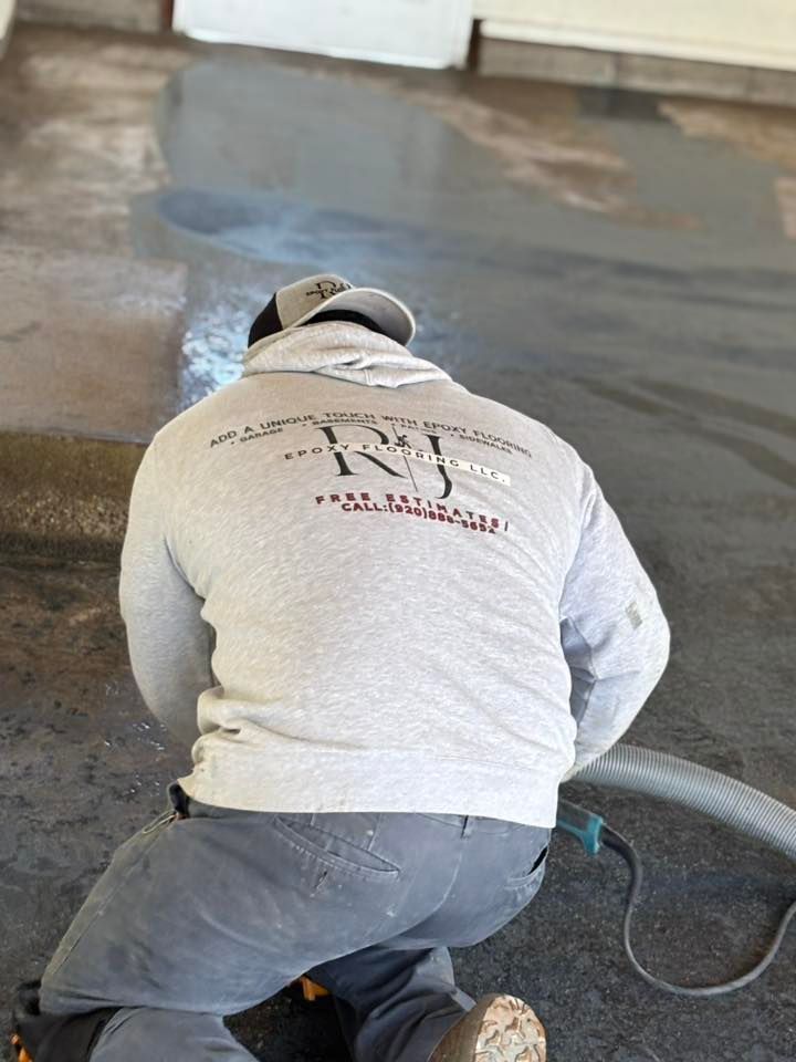 Person in a gray hoodie and cap kneeling, working on concrete, sparks flying, holding a tool.