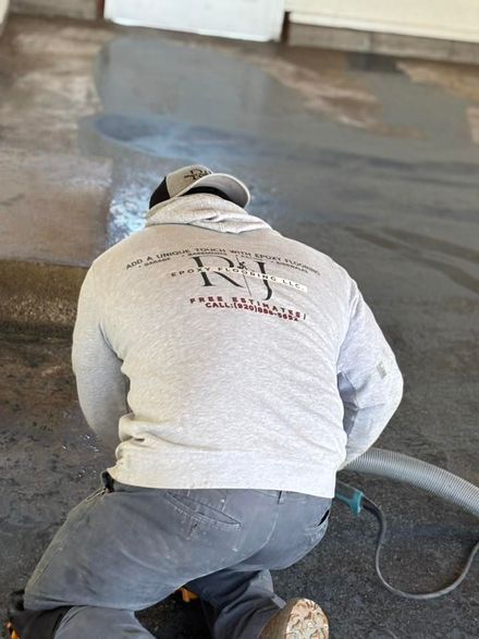 Person in a gray hoodie and cap kneeling, working on concrete, sparks flying, holding a tool.