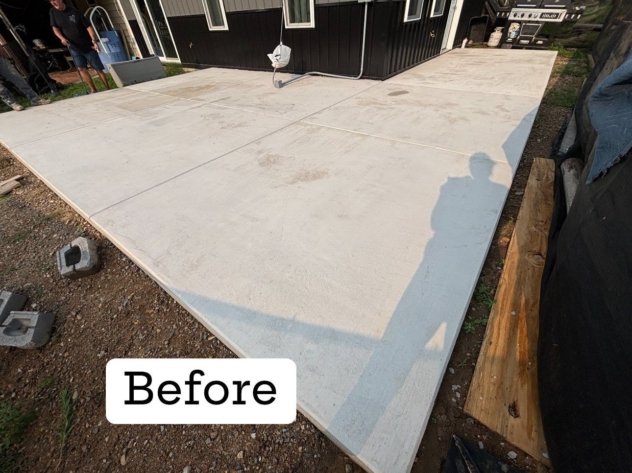 Newly poured concrete patio next to a black house; 