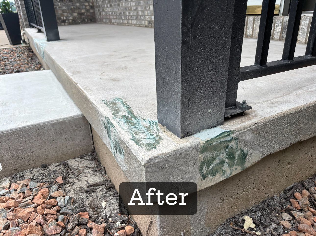 Concrete porch repair with green-tinted filler at the corner, black post and railing, gravel ground.