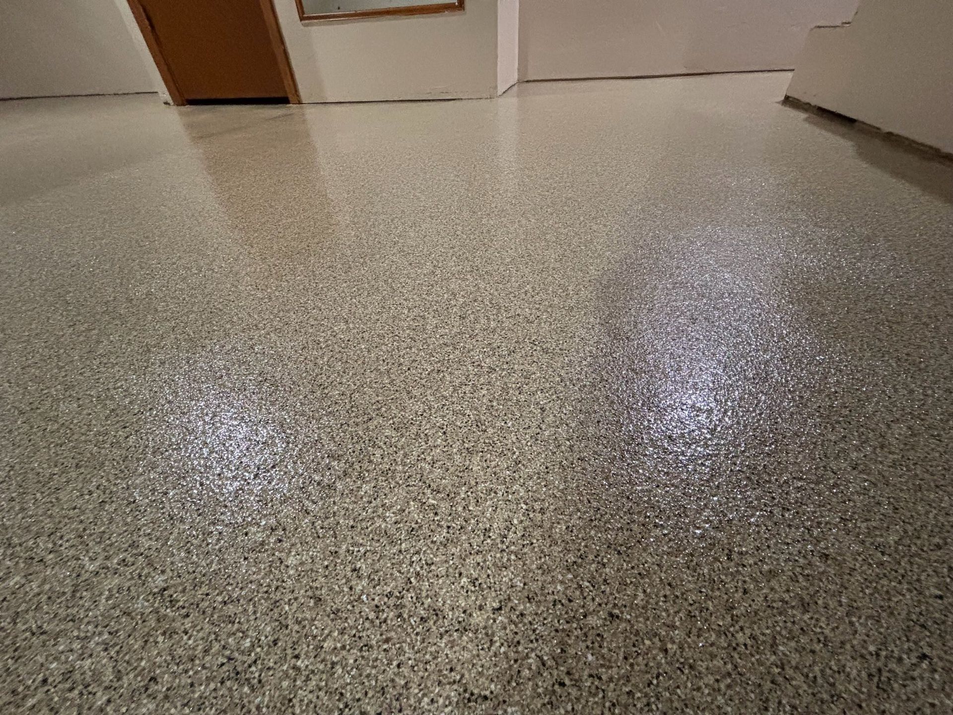 Epoxy-coated concrete floor with a speckled, light gray and white finish, reflecting light in a room.