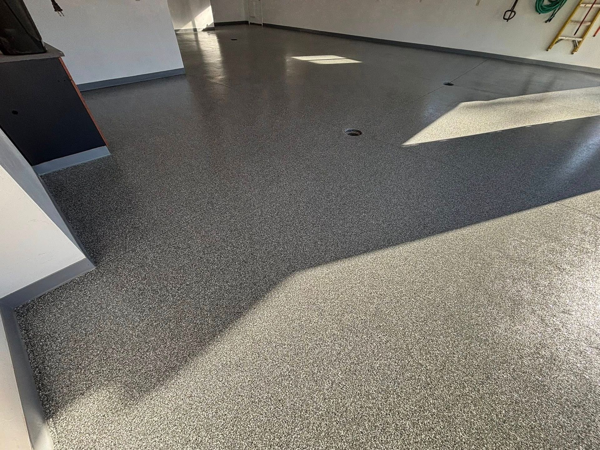 Shiny gray epoxy-coated garage floor with flecks. Sunlight reflects off the smooth surface.