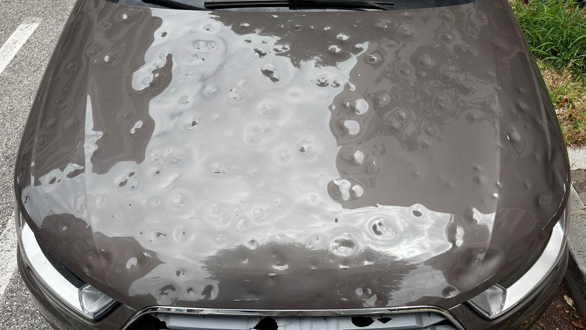 Car hood with heavy hail damage, showing multiple dents and surface impact marks.