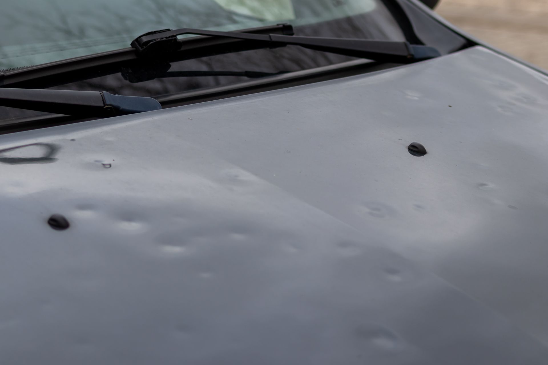 A car engine hood shows extensive hail damage dents across the surface. A car engine hood shows extensive hail damage dents across the surface.