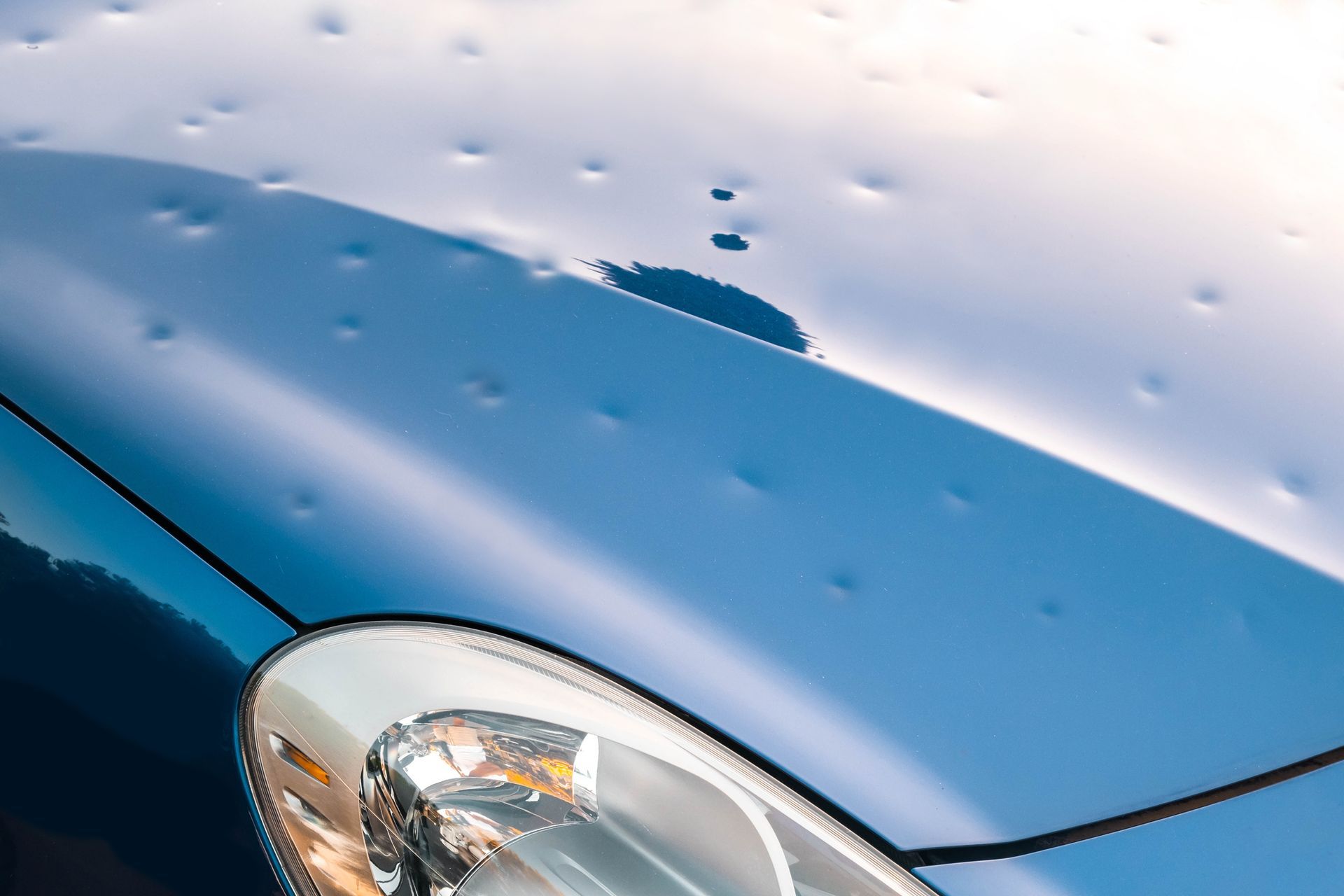 Close view of a dark-colored car hood with dents caused by a hail storm.